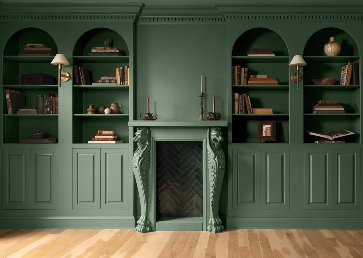 A green painted room with lower panelled walls and arched, built-in shelving topped with books and decor.
